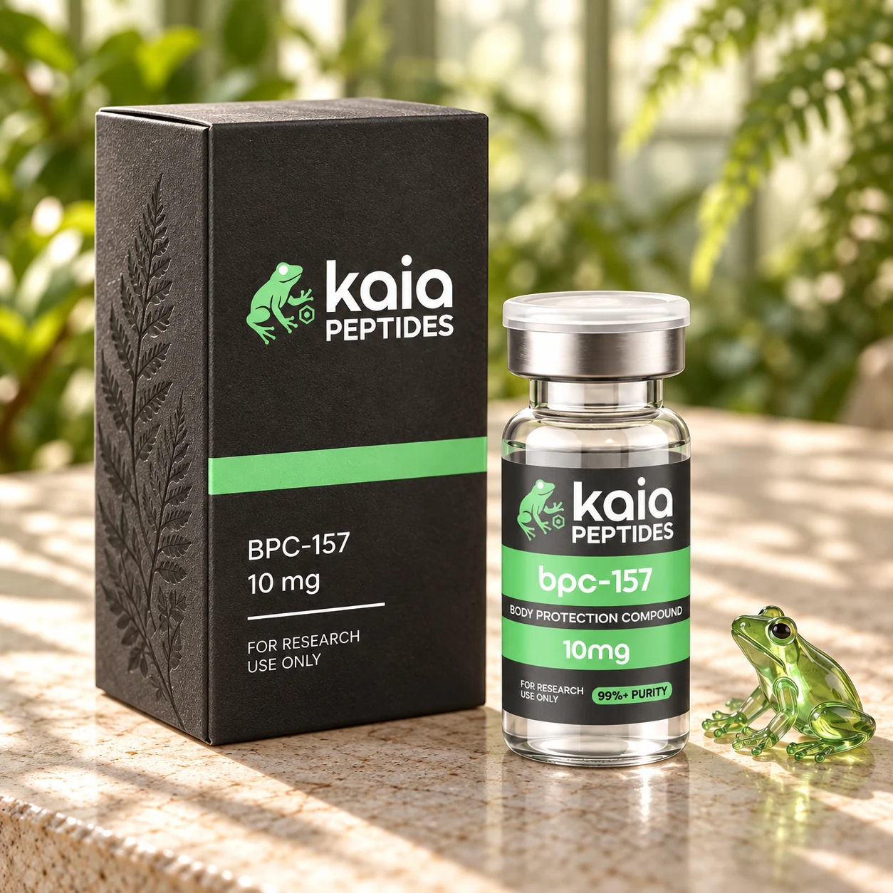 Close-up concept of the charcoal Kaia carton with a BPC-157 vial and small green glass frog